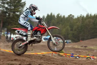 Motocross rider wearing a helmet and boots while jumping a dirt motorcycle