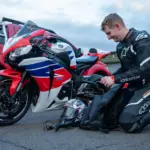 Motorcyclist in protective riding equipment beside a parked motorcycle