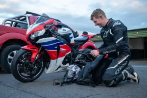 Motorcyclist in protective riding equipment beside a parked motorcycle