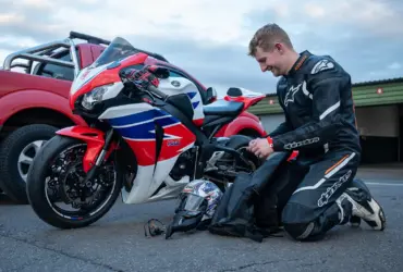 Motorcyclist in protective riding equipment beside a parked motorcycle