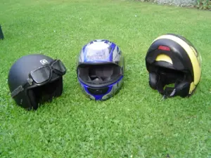 Three different styles of motorcycle helmet arranged on grass