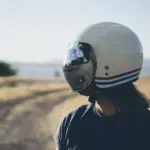Rider wearing a cream motorcycle helmet with a reflective visor