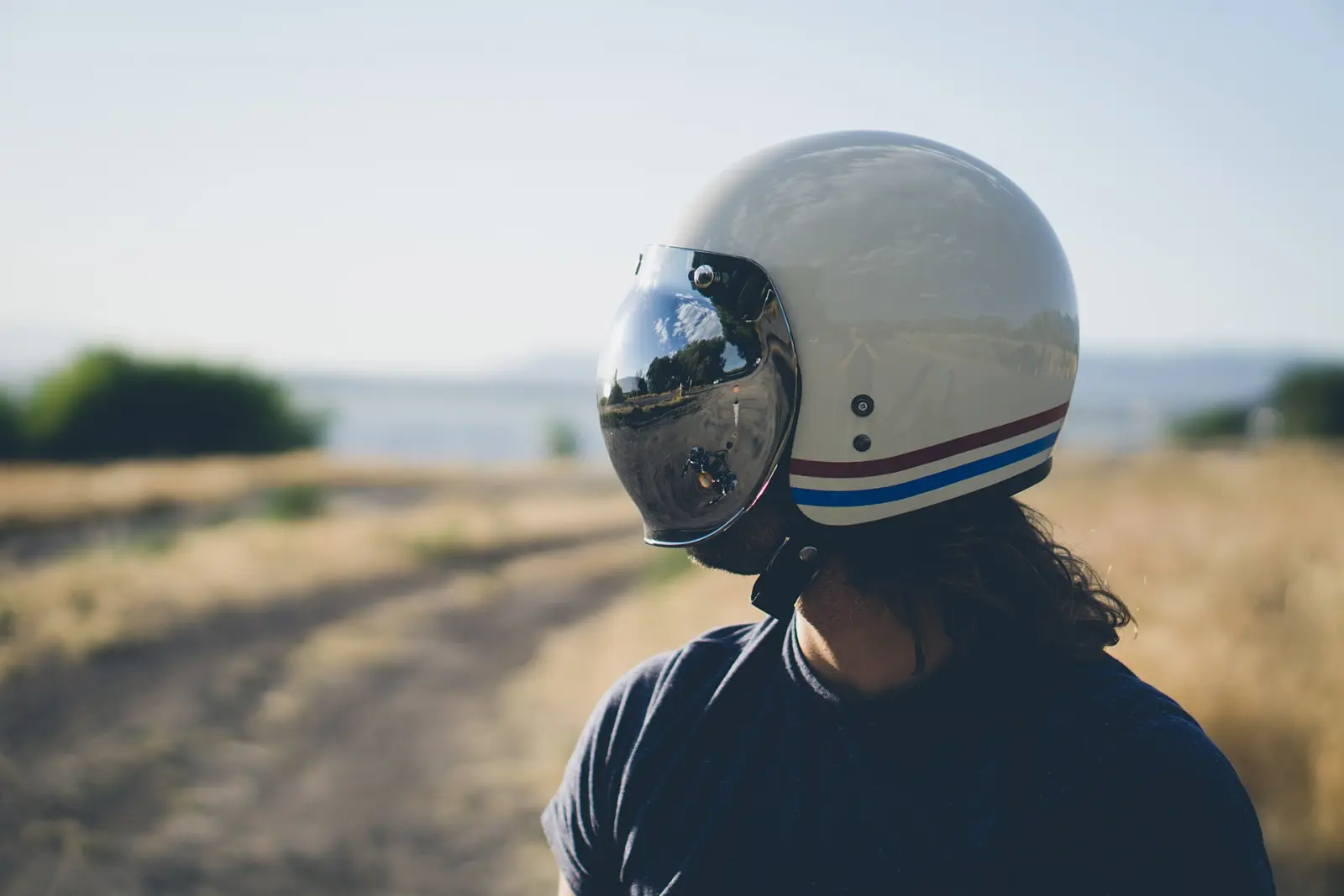 Rider wearing a cream motorcycle helmet with a reflective visor